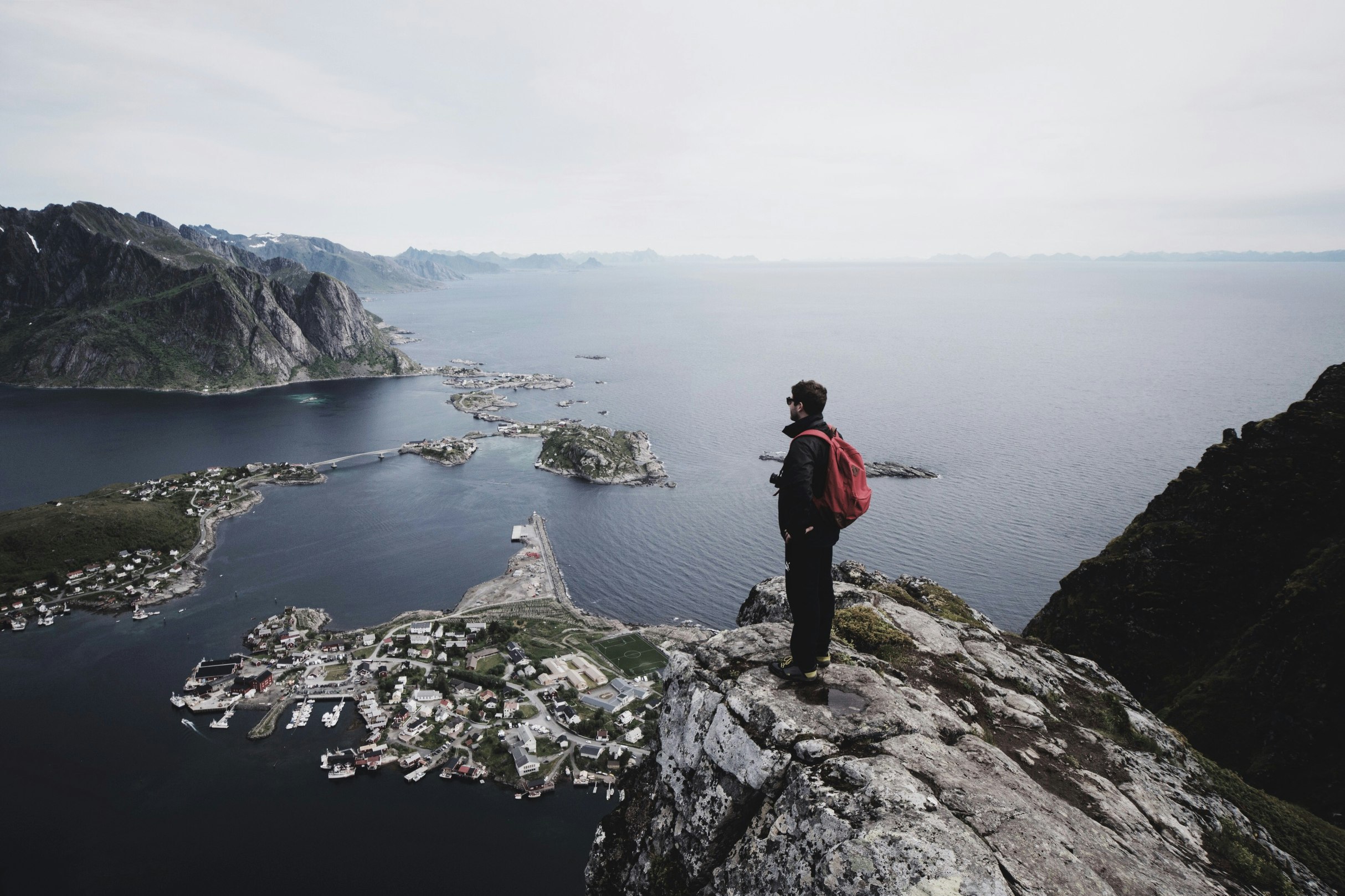 man standing on top of a cliff facing cityscape by water